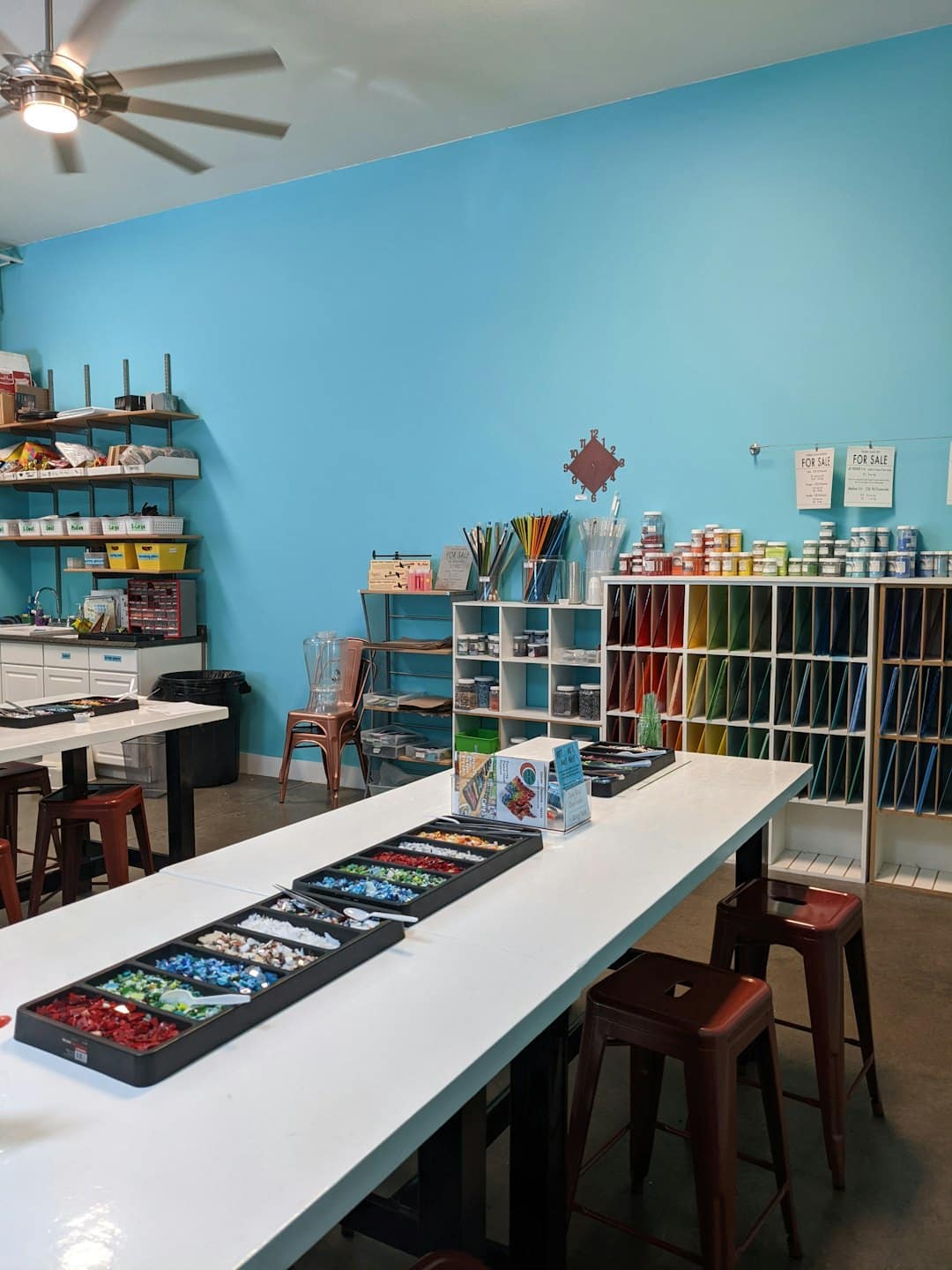 Laboratorio artigianale vuoto con tavoli ordinati e forniture di vetro colorato.