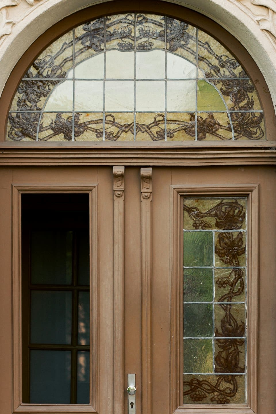 Porta in legno intarsiata con vetrate colorate in un arco beige.