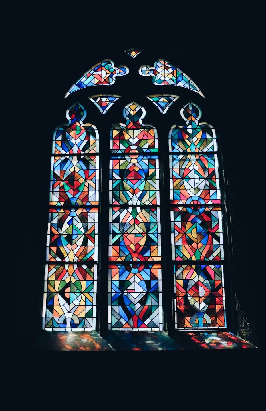 Finestra alta in vetro colorato illuminata da motivi geometrici colorati.